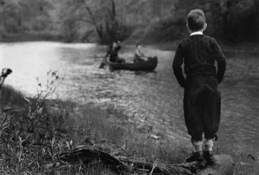 A boy on the shore looking at a canoe on the Des Plaines River