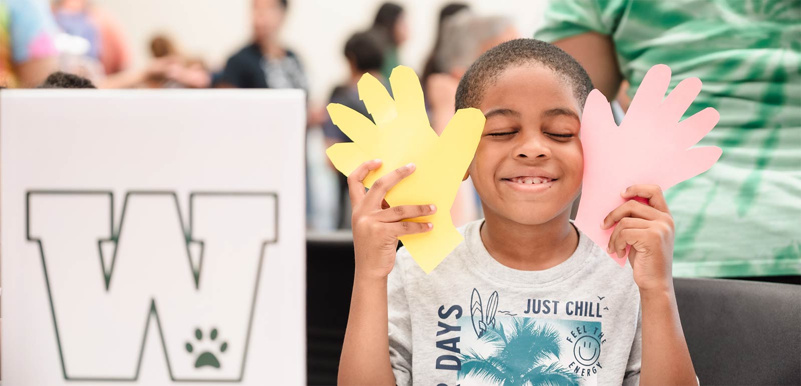 A boy closing his eyes and holding up two paper hands to his face