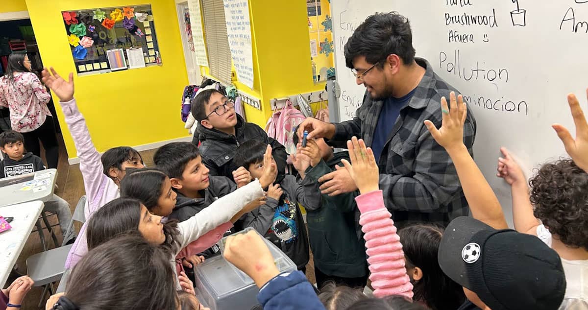 Eddie Flores holds a vial during a lecture on pollution as kids around him raise their hands