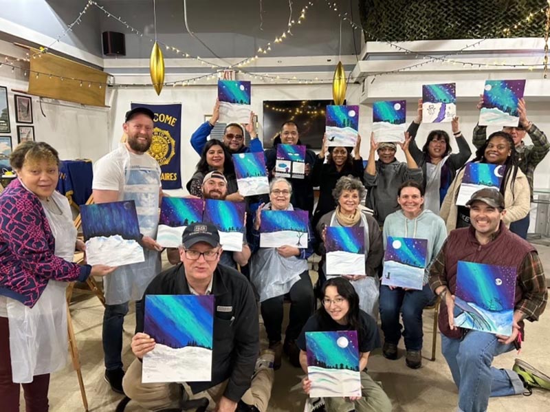 A group of veteran's hold up their painting of the northern lights.