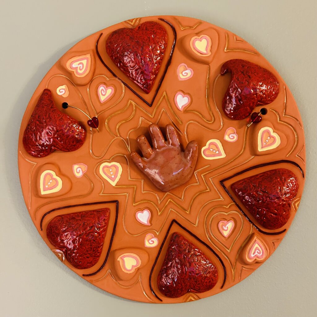 Clay sculpture with hearts surrounding a hand.