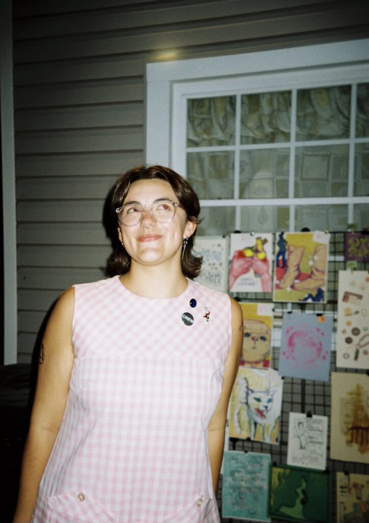 alexandra ok smiling in front of a rack of paintings