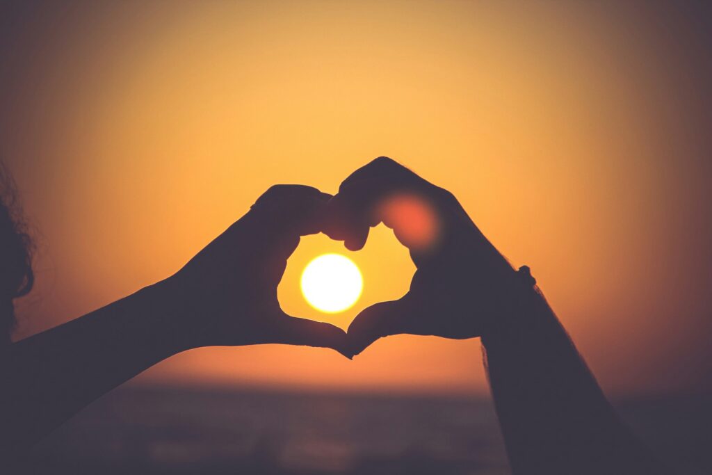Hands form a heart over a sunset