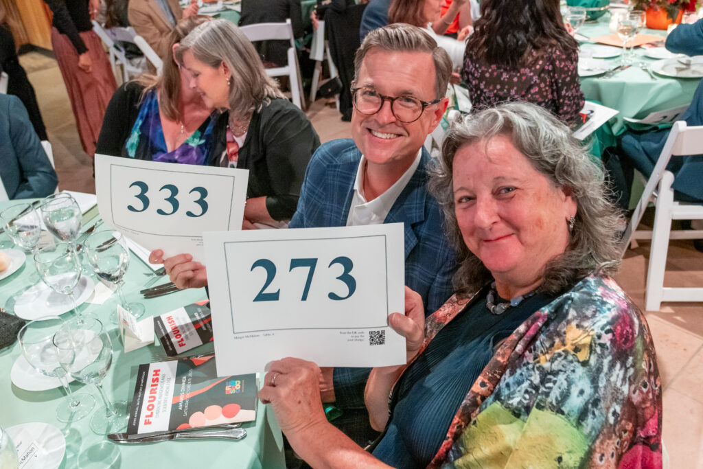 Two smiling guests hold up their paddle raise numbers. 