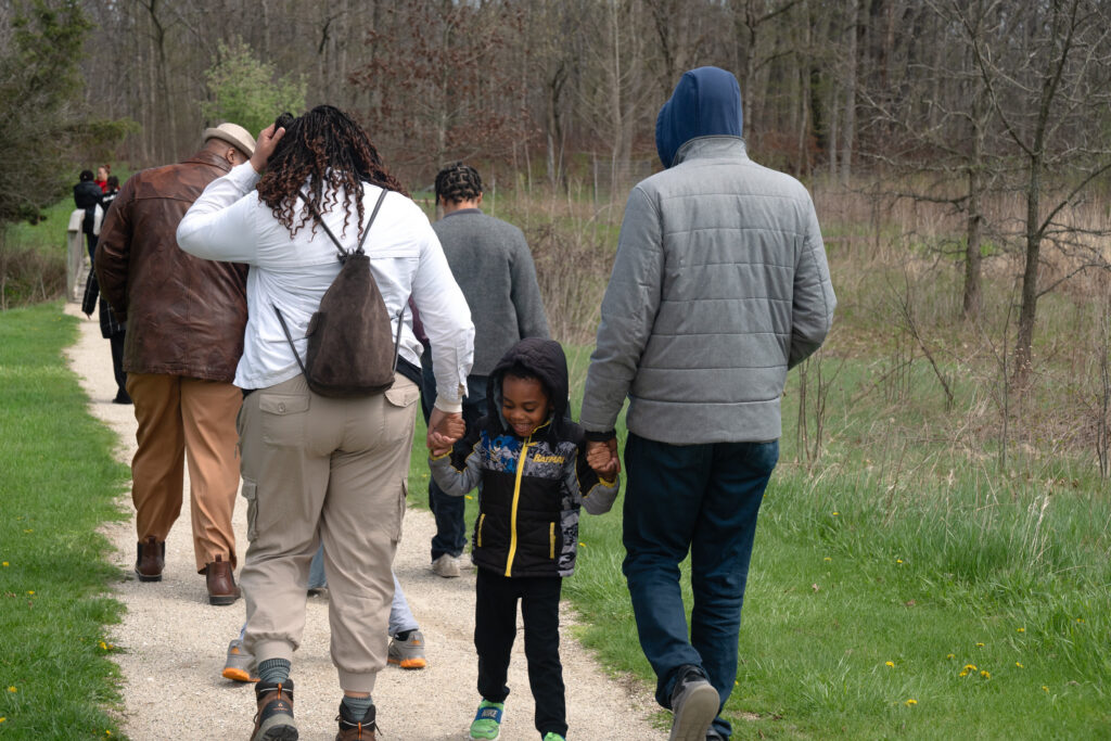 The group hikes at Ryerson Woods. A young child walks backwards between two adults.